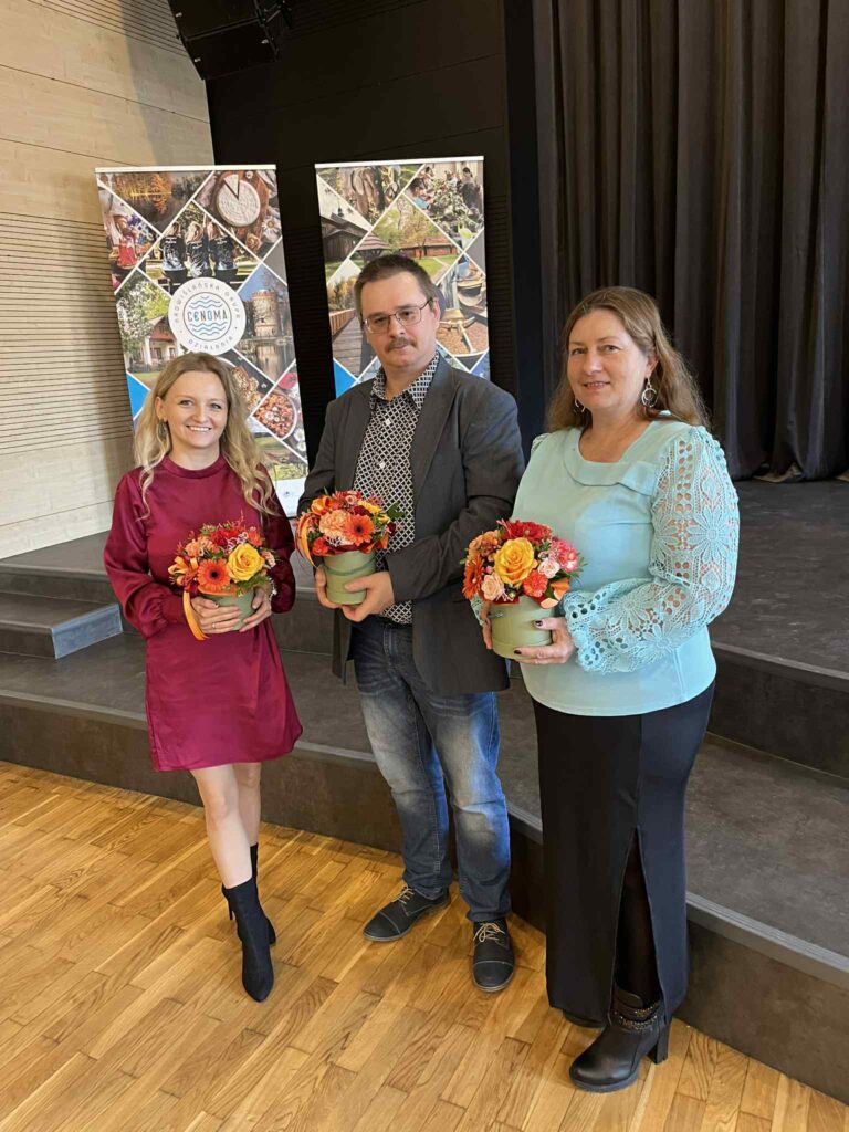 Zdjęcie przedstawiające Zarząd w trzech osobach na nową kadencję. Trzy osoby trzymają w rękach kwiaty - Justyna Boroń - Prezes Zarządu, - Anna Świątek - Skarbnik Zarządu, - Grzegorz Zarych - Wiceprezes zarządu. Za Zarządem stoją dwa banery.