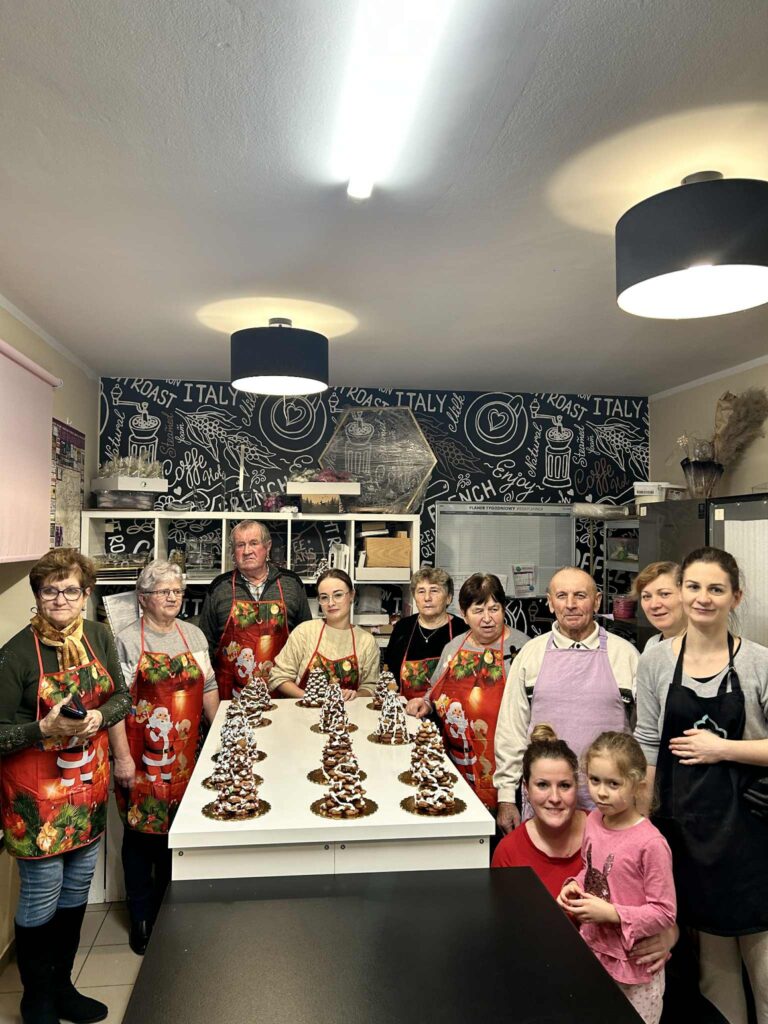 Zdjęcie przedstawiające wszystkich uczestników warsztatów wraz z Paniami cukiernikami oraz ich dzieła w postaci udekorowanych choinek bożonarodzeniowych