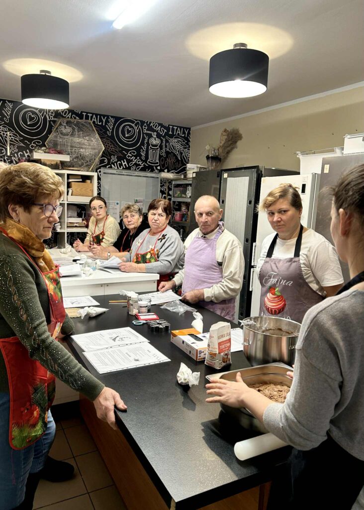 Uczestnicy warsztatów stoją przy stole wraz z Panią cukiernik